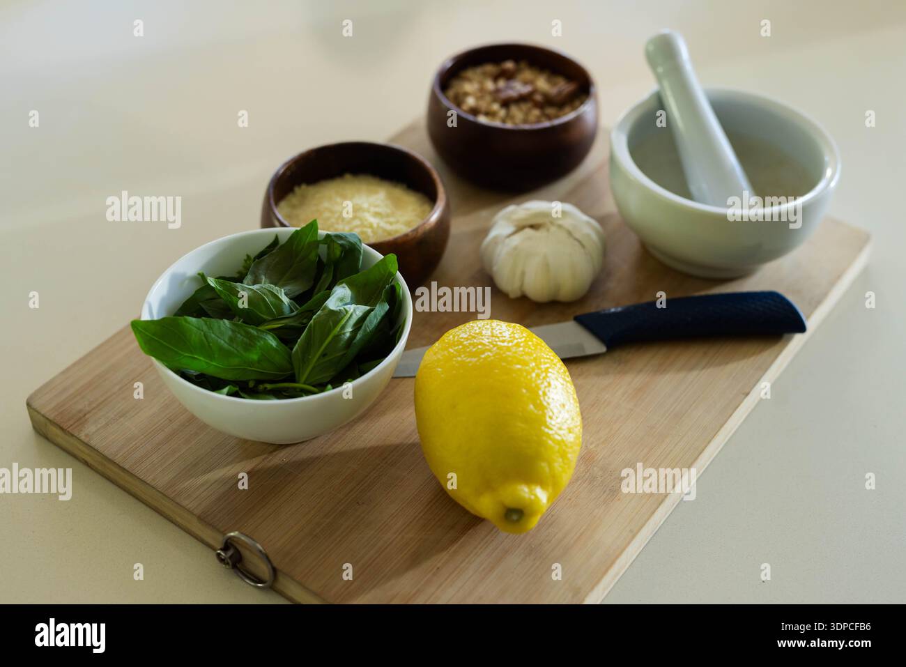 Whole lemon sitting on wooden cutting board with basil, paring knife, garlic, mortar Stock Photo