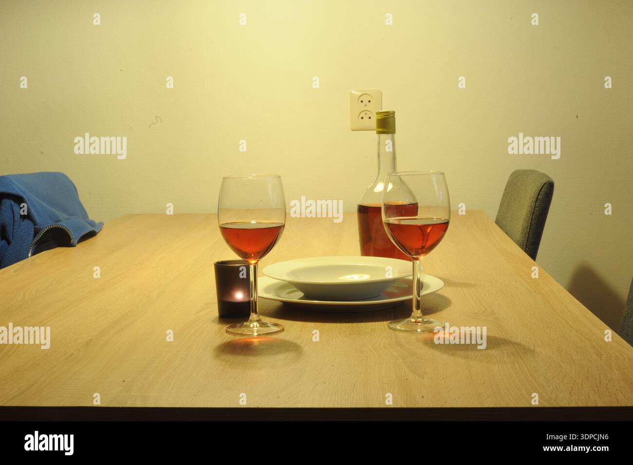 Romantic dinner setup featuring two wine glasses, a bottle of rosé, a lit candle and plates on a wooden table creating an intimate, cozy atmosphere. Stock Photo