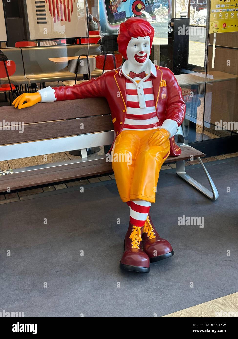 McDonalds restaurant Ronald McDonald figure life size statue likeness sitting on a bench outside a McDonald's in Maryland. - Smartphone Captured Stock Image
