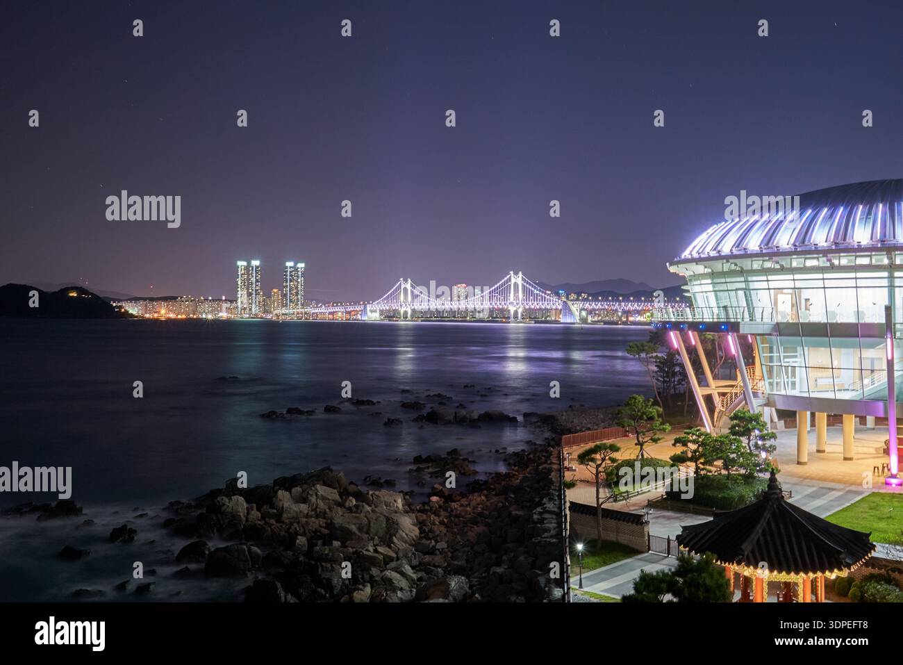 A serene nighttime long exposure of the illuminated Nurimaru APEC House on Dongbaekseom Island, featuring the Gwangan Bridge and the Busan city Stock Photo