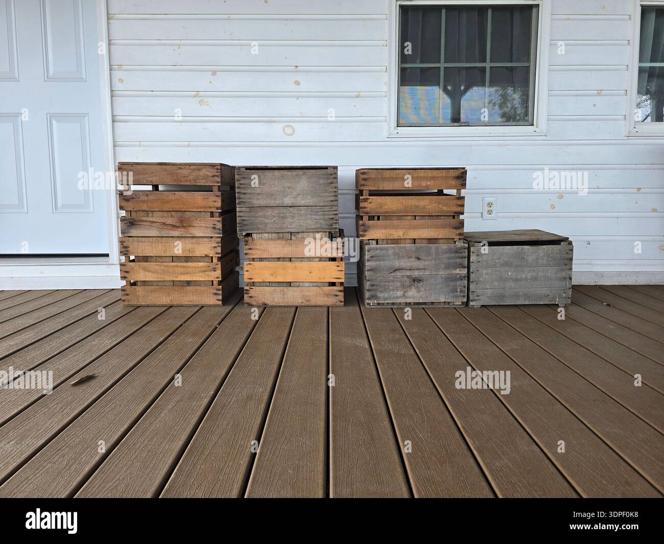 Rustic wooden crates displayed on a wooden porch in front of a white wall - Smartphone Captured Stock Image