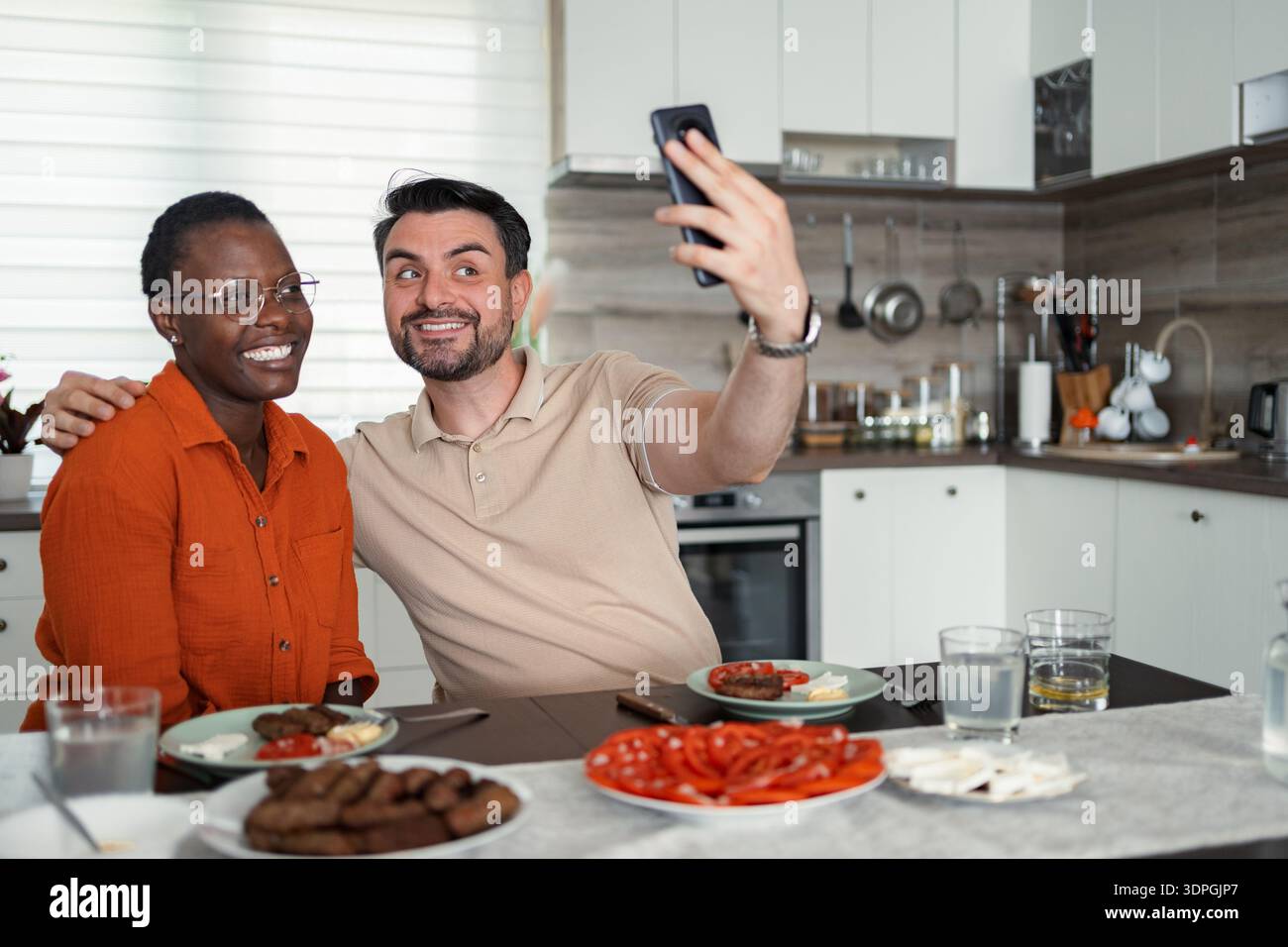 Happy multi-ethnic couple taking a selfie while having lunch in the kitchen Stock Photo