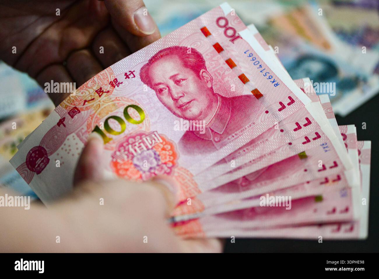In this photo illustration, a hand fans out a stack of 100-yuan RMB ...