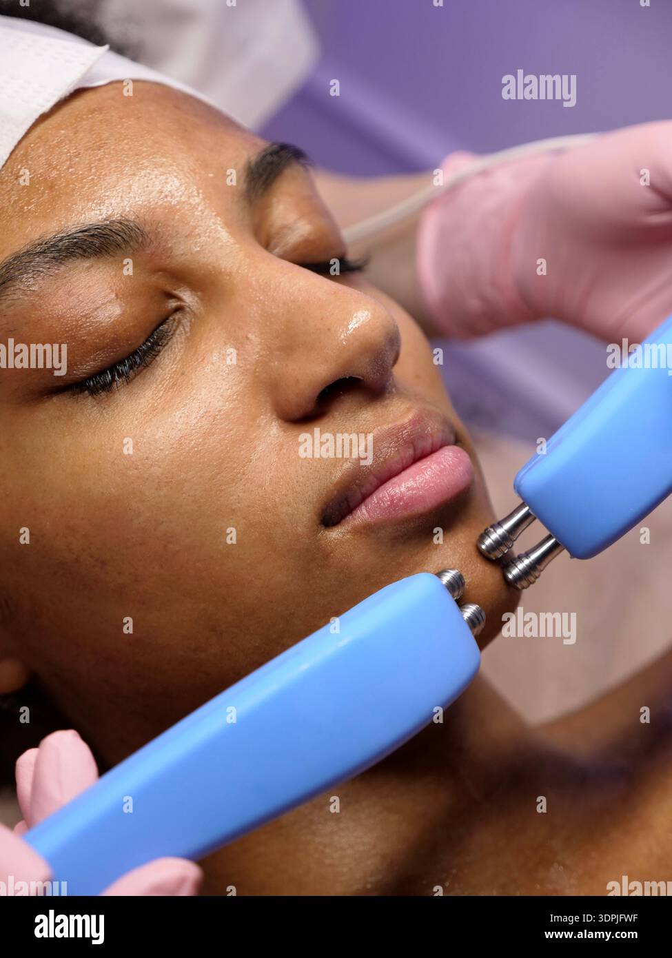 African American female receiving microcurrent therapy to improve skin elasticity and hydration. Professional anti-aging hardware cosmetology service. Stock Photo