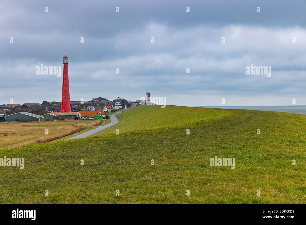 The iconic red lighthouse Lange Jaap in Huisduinen, Den Helder, standing tall behind the sea dike under a dramatic sky. Tallest cast-iron tower. Stock Photo