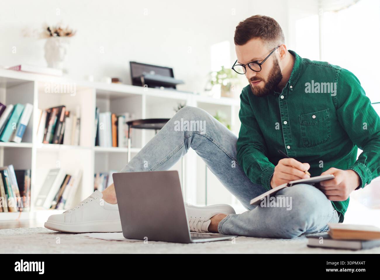 Millennial Guy Writing Taking Notes Looking At Laptop At Home Stock Photo