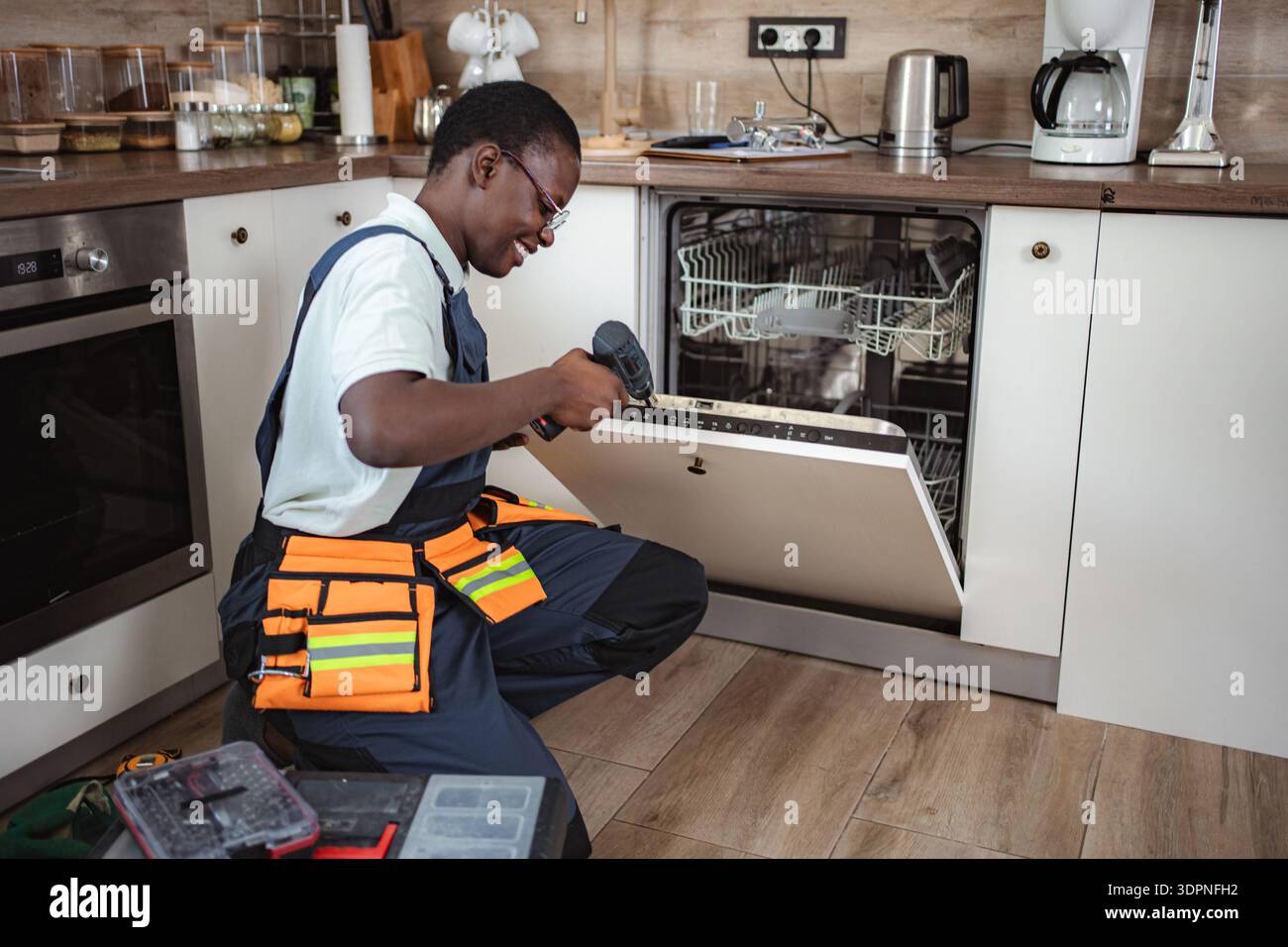 Technician repairing dishwasher using electric screwdriver in kitchen Stock Photo