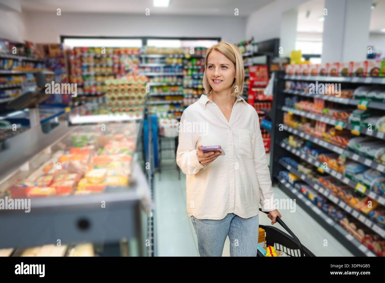 Woman using phone for shopping list in supermarket aisle Stock Photo