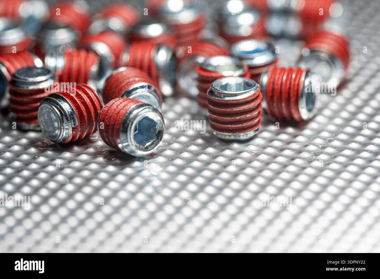 close up of ndustrial grub screws with red thread locker coating scattered on a textured metallic surface featuring selective focus and technical Stock Photo