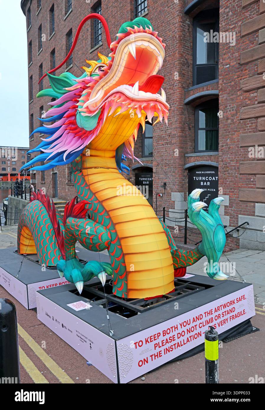 Illuminated Chinese New Year dragon lantern installation at Royal Albert Dock, Liverpool, beside historic brick warehouses. Stock Photo