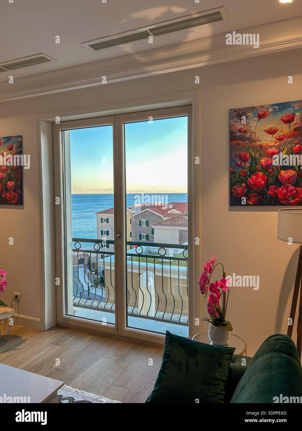 Modern living room interior with balcony doors opening to a scenic sea view and coastal houses at sunset. - Smartphone Captured Stock Image