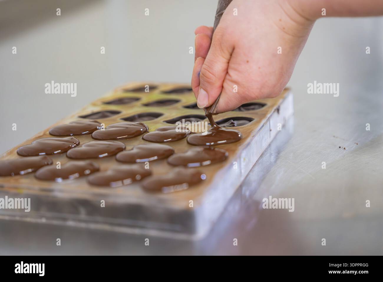 Hand fills chocolate into a chocolate mold lying on a table, vegan ...