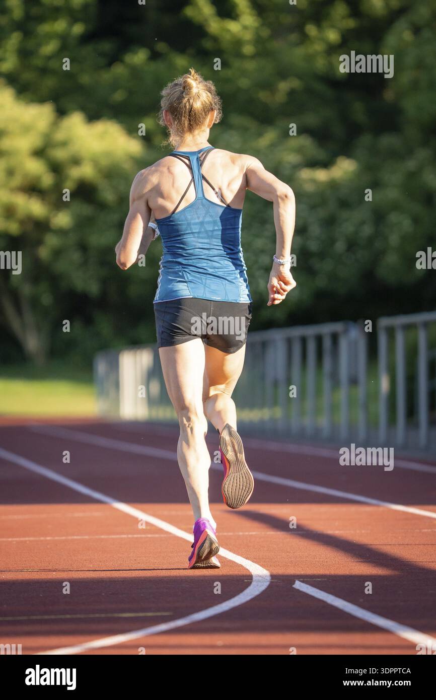 Back view of a running athlete on a red track surrounded by nature ...