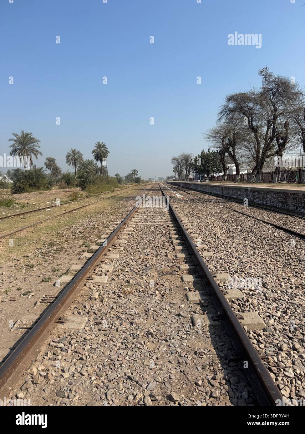 Rural Railway Tracks with Empty Platform Under Clear Blue Sky - Smartphone Captured Stock Image