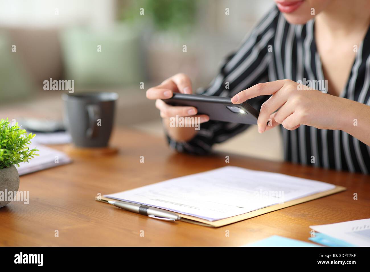 Close up of a self employed hands taking photo of contract or form with smart phone working at home Stock Photo