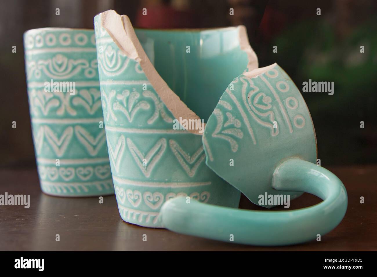 Broken turquoise ceramic cup with handle pieces on wooden table surface Stock Photo