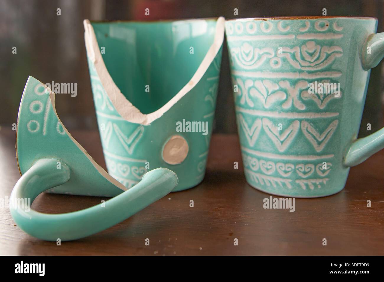 Broken turquoise ceramic cup with handle pieces on wooden table surface Stock Photo