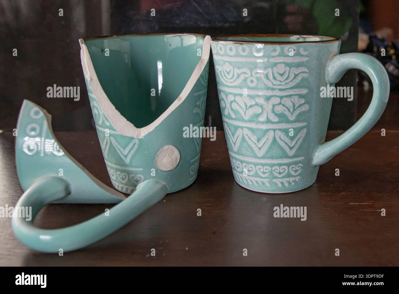 Broken turquoise ceramic cup with handle pieces on wooden table surface Stock Photo
