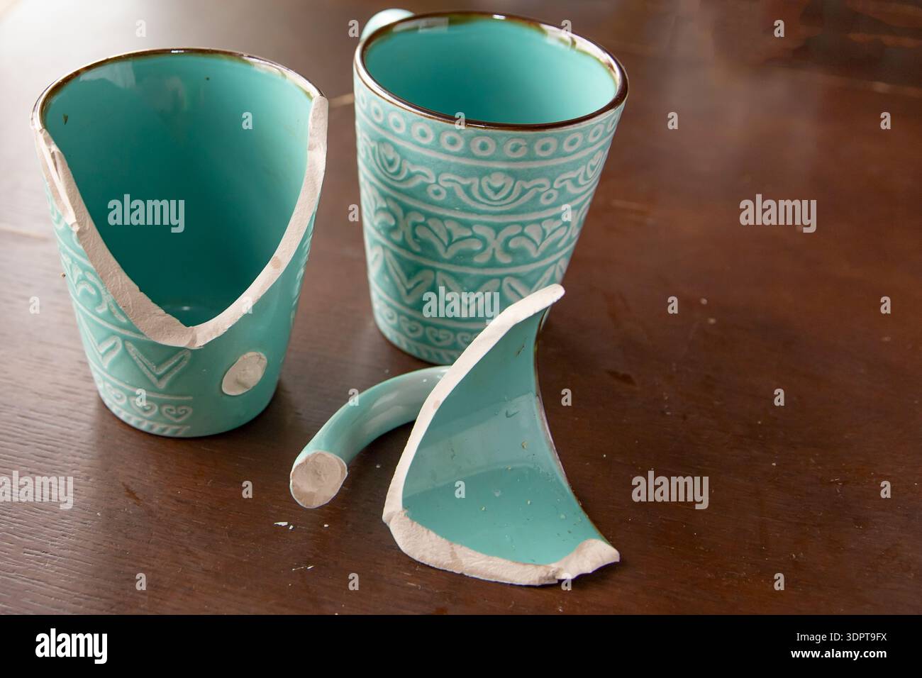 Broken turquoise ceramic cup with handle pieces on wooden table surface Stock Photo