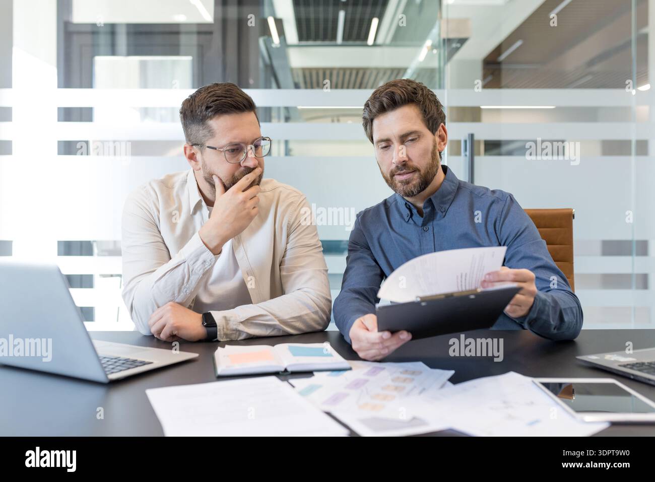 Experienced businessmen analyzing corporate financial reports, reviewing important documents, and discussing a new project contract during an official business meeting in a modern office Stock Photo