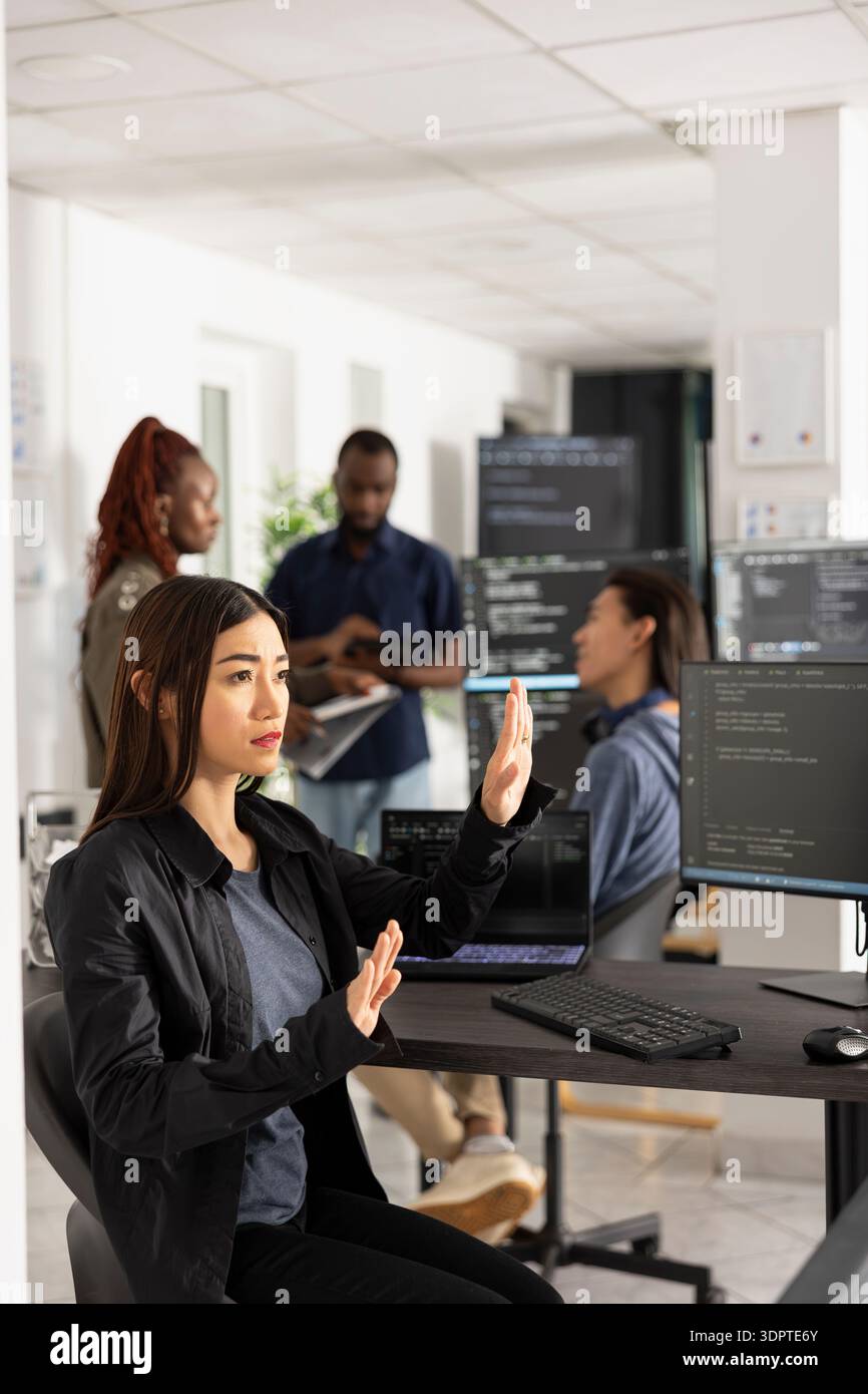 Asian female programmer works with 3D interface in modern office, testing code for app development. Woman doing hand gestures while interacting with holographic screen, analyzing website performance. Stock Photo