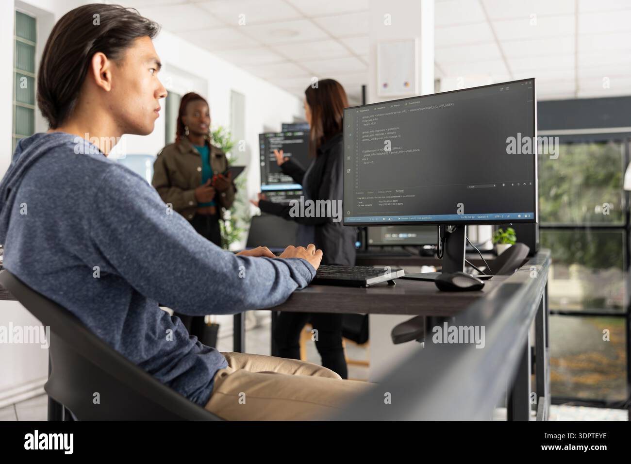 Asian male developer works diligently to improve applications, reviewing backend data on computer. Young adult programmer analyzes HTML coding scripts and focuses on problem solving and optimization. Stock Photo