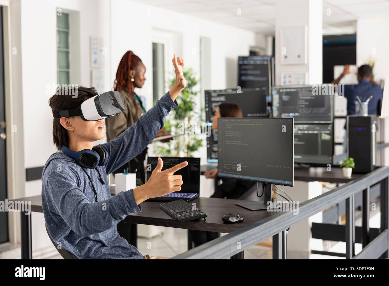 Asian software developer wears VR glasses and interacts with virtual 3D programming environment. The scene highlights cutting edge technology, coding analysis and innovation in software development. Stock Photo