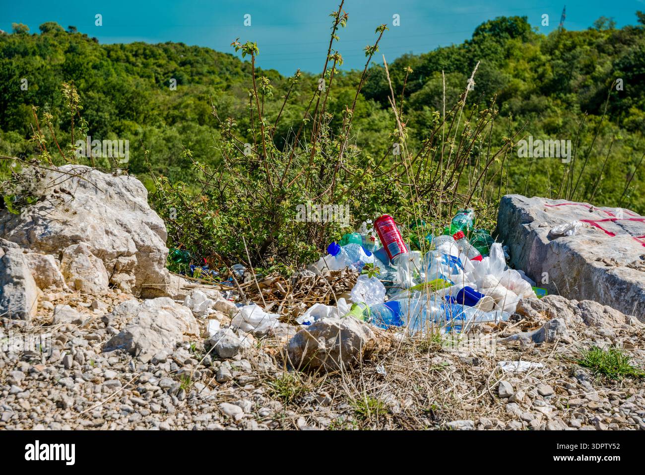 Plastic waste scattered among rocks in a natural setting. Lush greenery ...