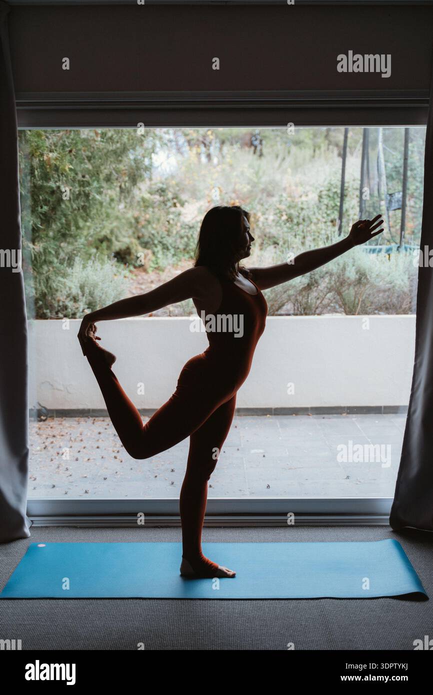 Woman Practicing Yoga in Dancer Pose by a Window Stock Photo