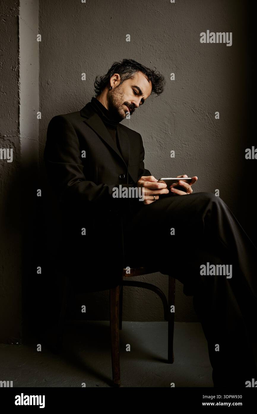 Elegant man in black suit using smartphone in dark studio Stock Photo