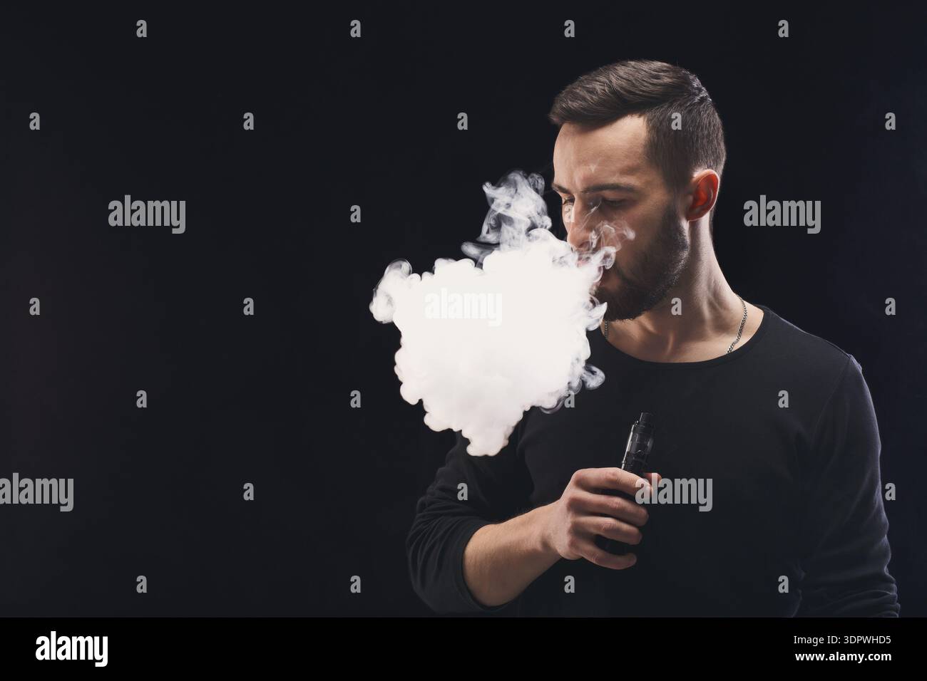 holding in vape smoke Man Exhales Vapor While a Device a Dark Setting During an Indoor Session Stock Photo Color:Red buy geek bar near gpriv 2