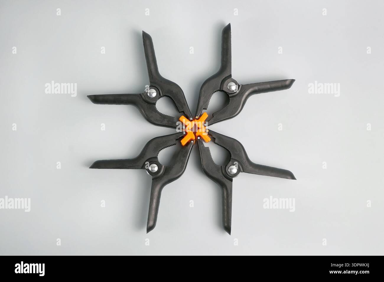 Four black plastic spring clamps with orange pads arranged in circle, isolated on white. Strong grip hand tools for woodworking, DIY, repair and works Stock Photo
