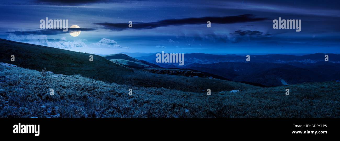mountainous panorama of rolling hills at night. wonderful weather with cloudscape over the distant mountain range in full moon light. mysterious view Stock Photo