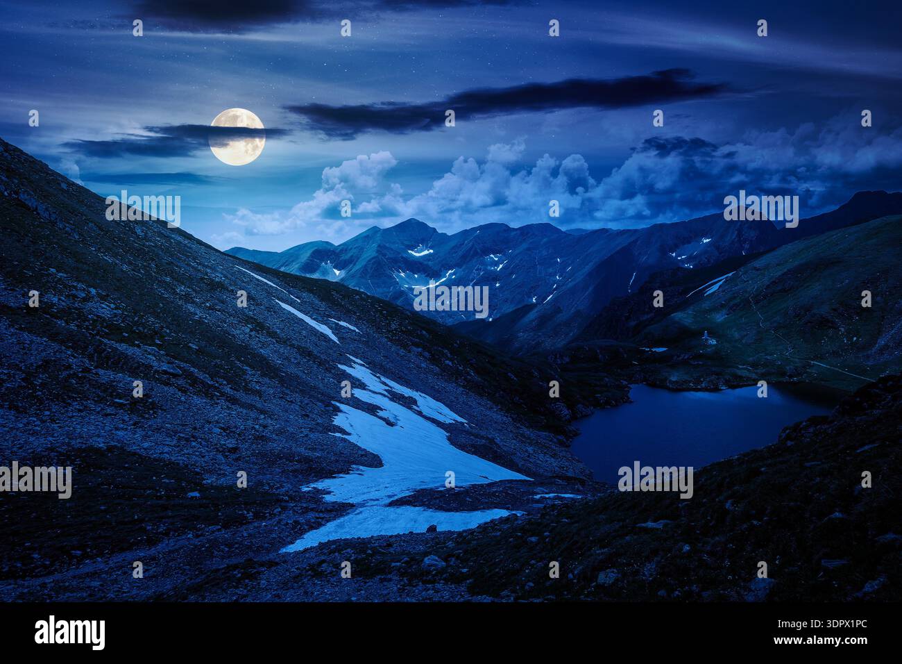 mountain lake in alpine summer landscape at night. beautiful view surrounded with clouds on a dark sky in full moon light. fresh water, snow and rocky Stock Photo
