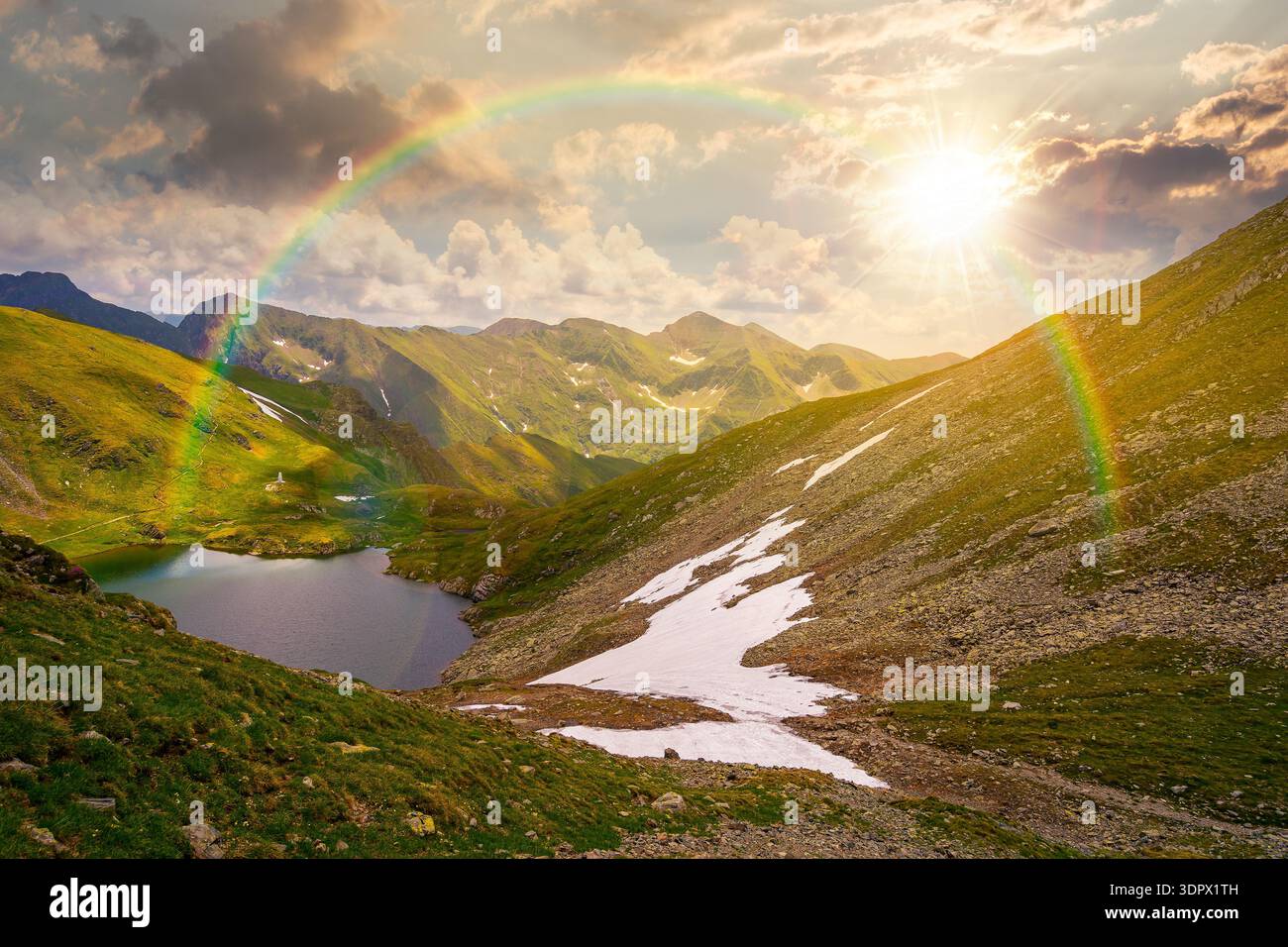 mountain lake in alpine summer landscape at sunset. beautiful view surrounded with clouds on a blue sky in evening light. fresh water, snow and rocky Stock Photo
