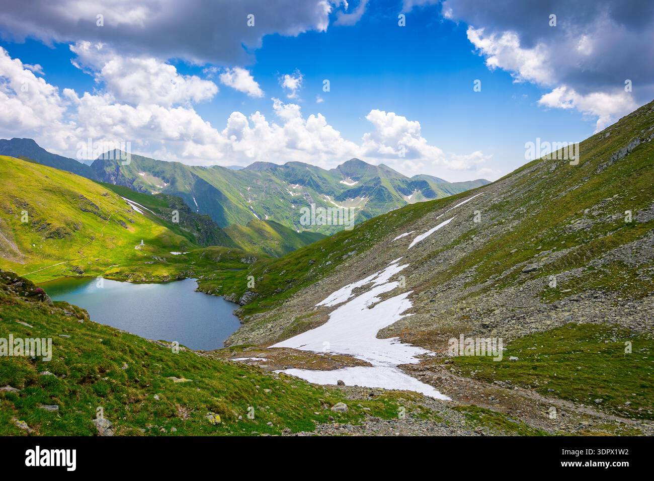 mountain lake in alpine summer landscape. beautiful view surrounded with transylvania alps and clouds on a blue sky. fresh water, snow and rocky slope Stock Photo