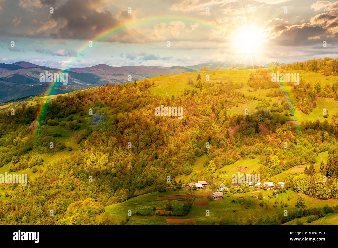 beautiful rural area in mountain landscape at sunset. village on a steep green hill during spring in evening light. alpine countryside scenery in dapp Stock Photo