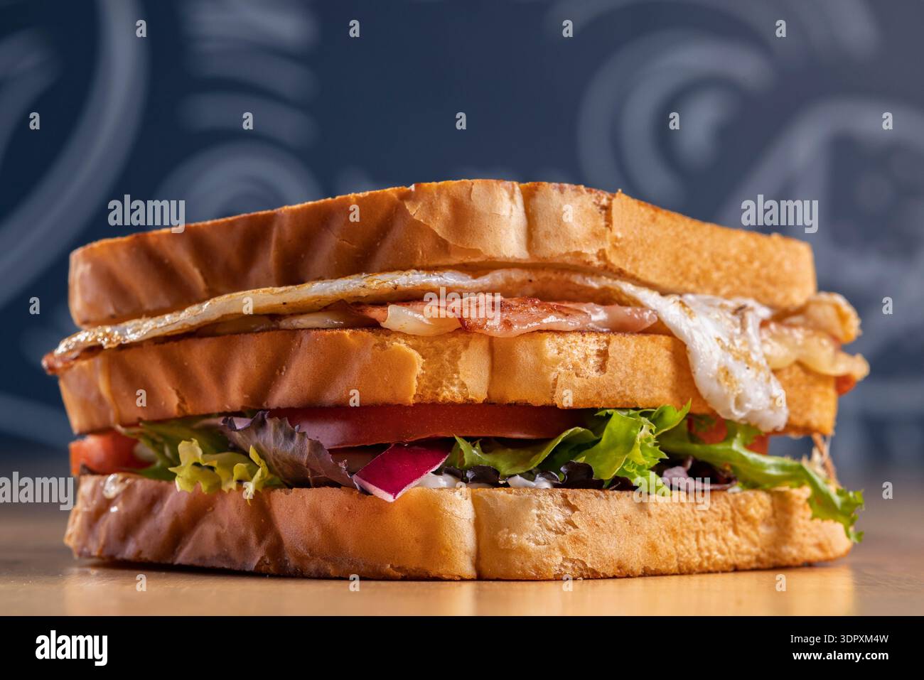 Mouthwatering ham and cheddar sandwich stacked with crispy fried egg, fresh lettuce, juicy tomato, and sliced onion, served on toasted bread for a del Stock Photo