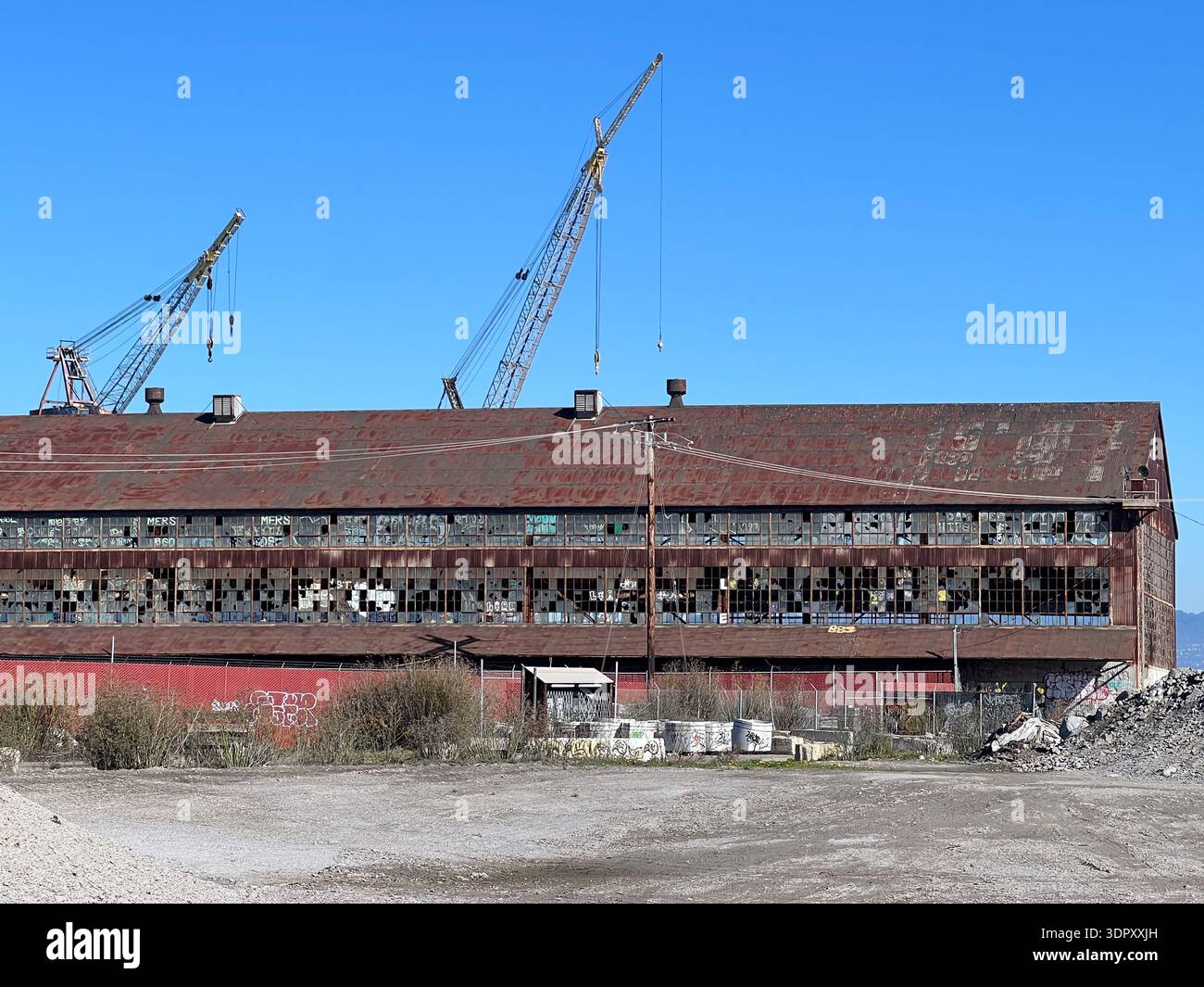 A long industrial building with two cranes behind it displays a vast collection of broken windows in two narrow bands - Smartphone Captured Stock Image