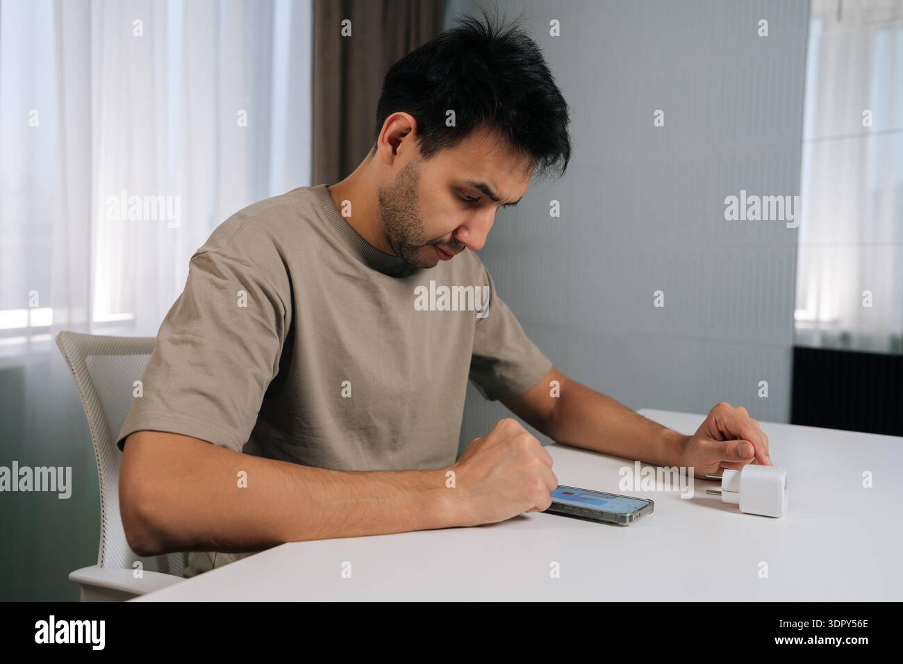 Focused man connecting smart home device using smartphone, looking at application settings, setting up and controlling smart socket from mobile app Stock Photo