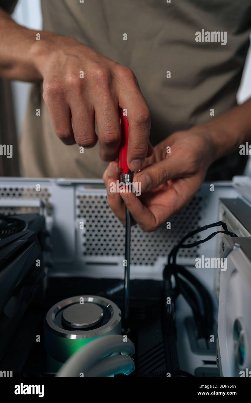 Technician hands maintaining and upgrading a personal computer, assembling internal hardware components with screwdriver, performing service and Stock Photo