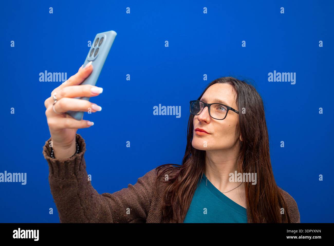 Woman holding smartphone, taking selfie. Wearing eyeglasses, capturing digital content for social media and online communication Stock Photo