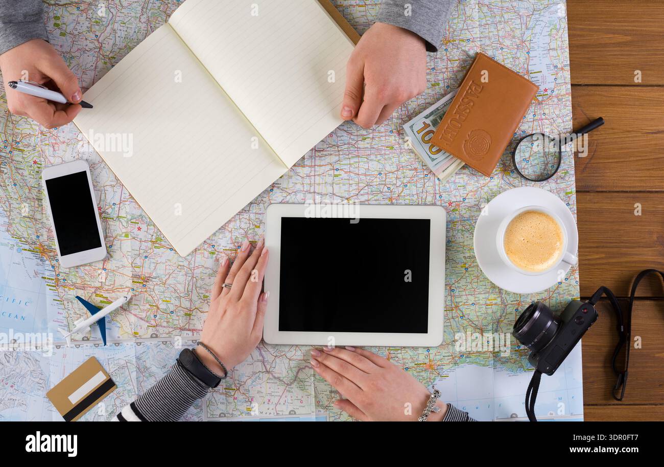 Group Planning a Trip Using Map, Tablets, and Notes at a Wooden Table With Coffee Stock Photo