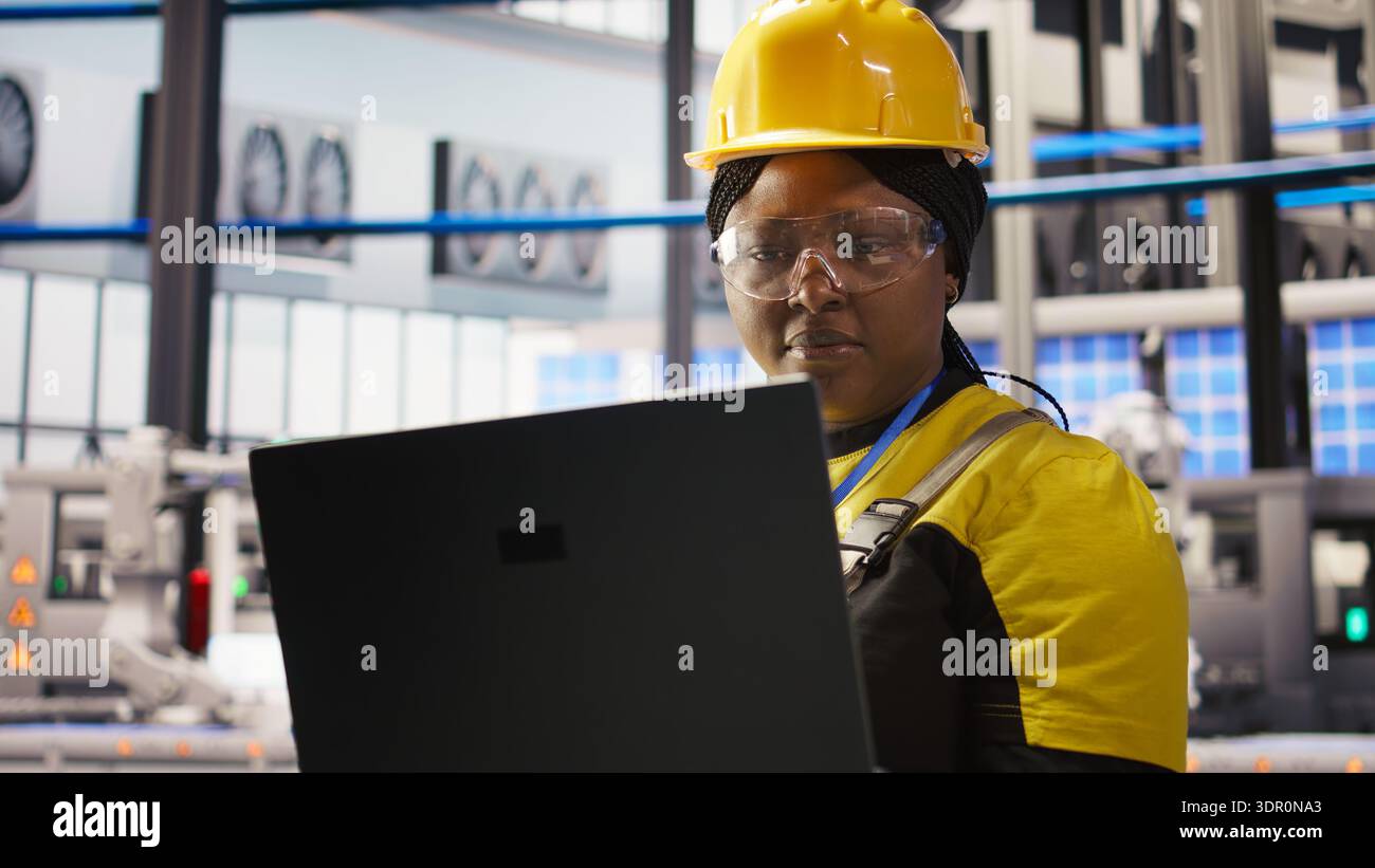 Solar panels plant technician uses laptop to oversee systems, ensuring machinery operates at optimal efficiency. Photovoltaics plant employee uses software on notebook to maintain operations, camera A Stock Photo