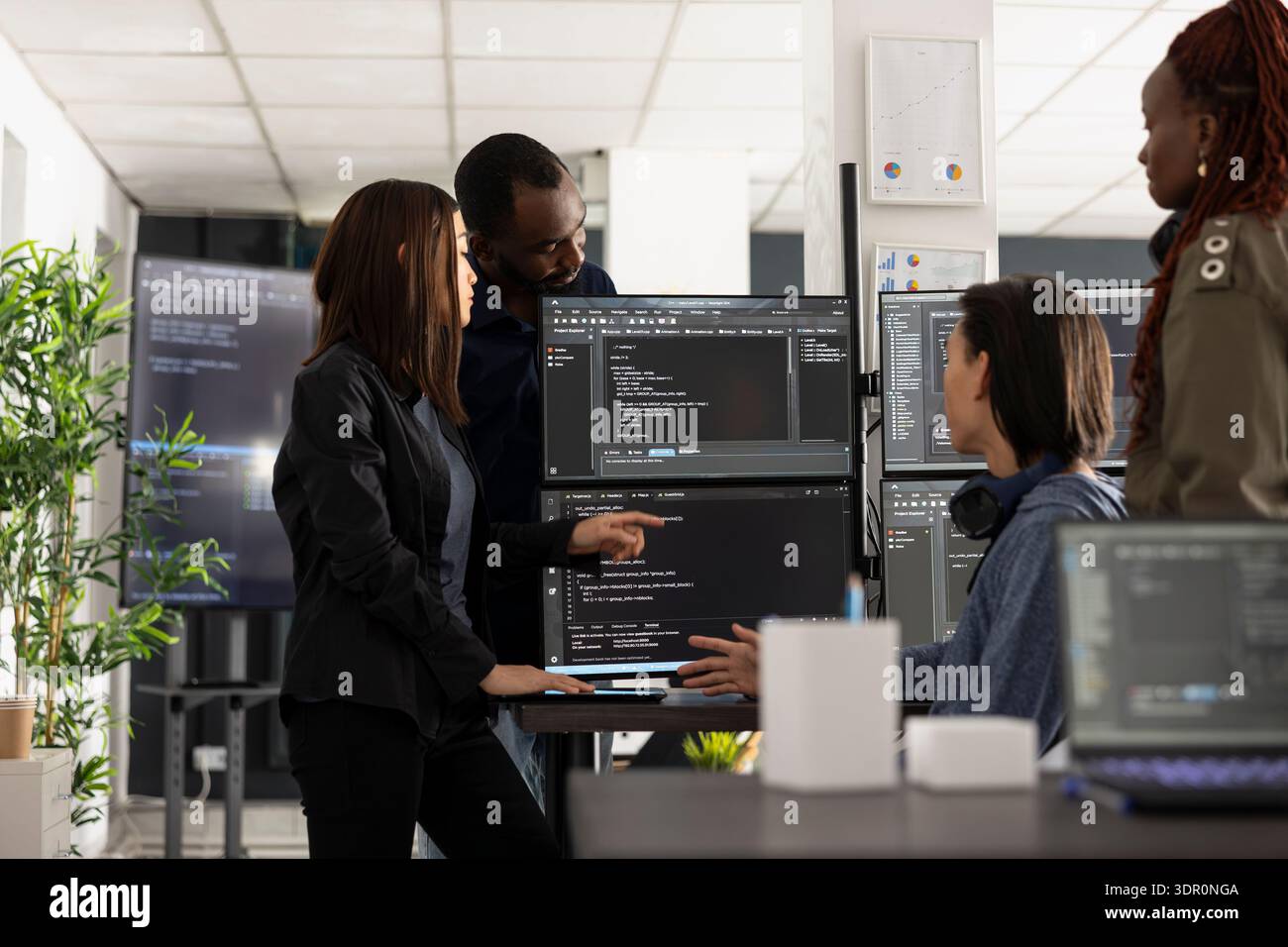 Professional programmers collaborate in tech workspace, analyzing coding scripts on computer monitors. Diverse male and female developers discussing app development and website solutions. Stock Photo