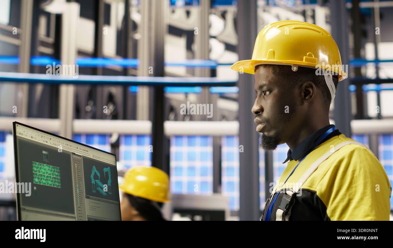 Smart factory employee typing on PC keyboard, testing automated systems, doing maintenance. Industry 4.0 plant staff member using computer to inspect equipment and repair bugs, camera B Stock Photo
