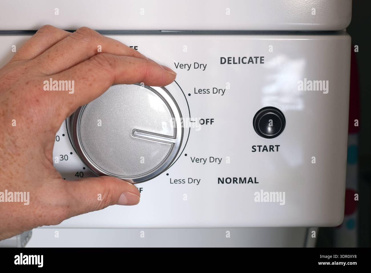Closeup of person’s hand turning dial, adjusting settings on household clothes dryer control panel. Home laundry routine concept featuring appliance o Stock Photo