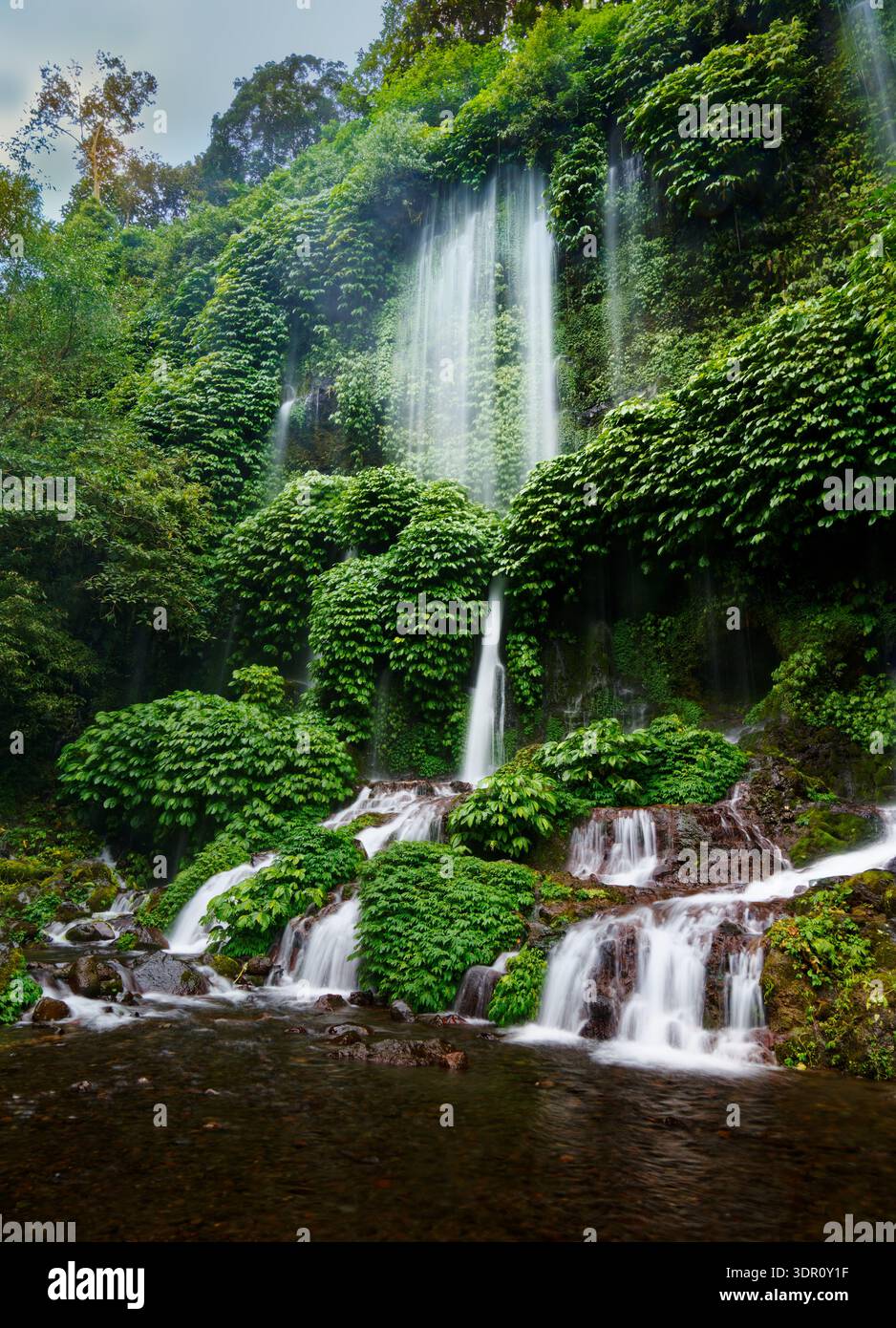 Air Terjun Benang Stokel waterfall, Lombok, Indonesia — thin streams cascade over mossy cliff in lush tropical rainforest, dense green vegetation, mis Stock Photo