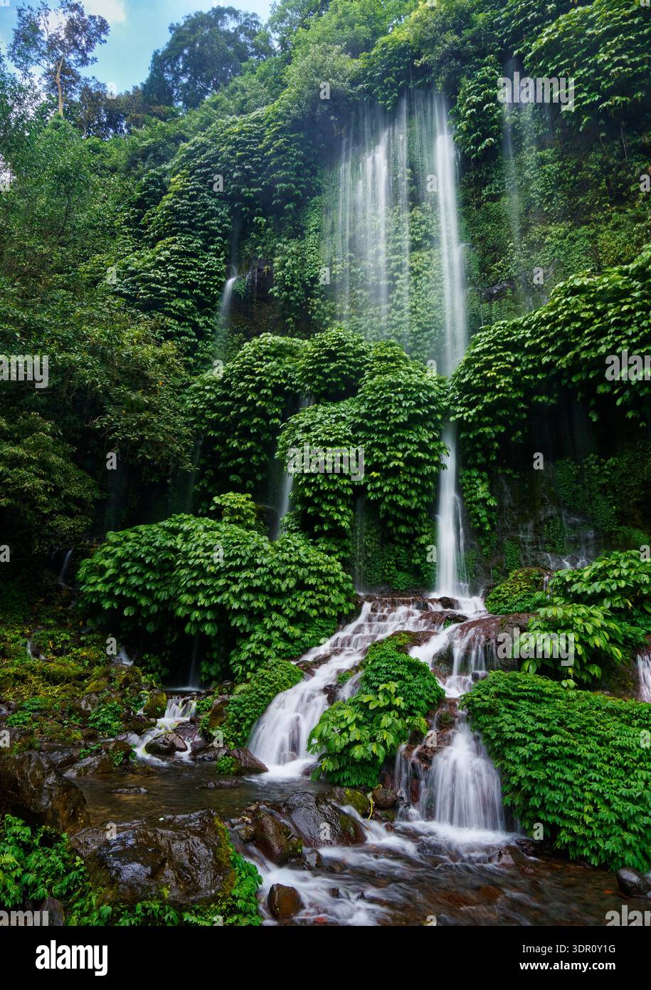 Air Terjun Benang Stokel waterfall, Lombok, Indonesia — thin streams cascade over mossy cliff in lush tropical rainforest, dense green vegetation, mis Stock Photo