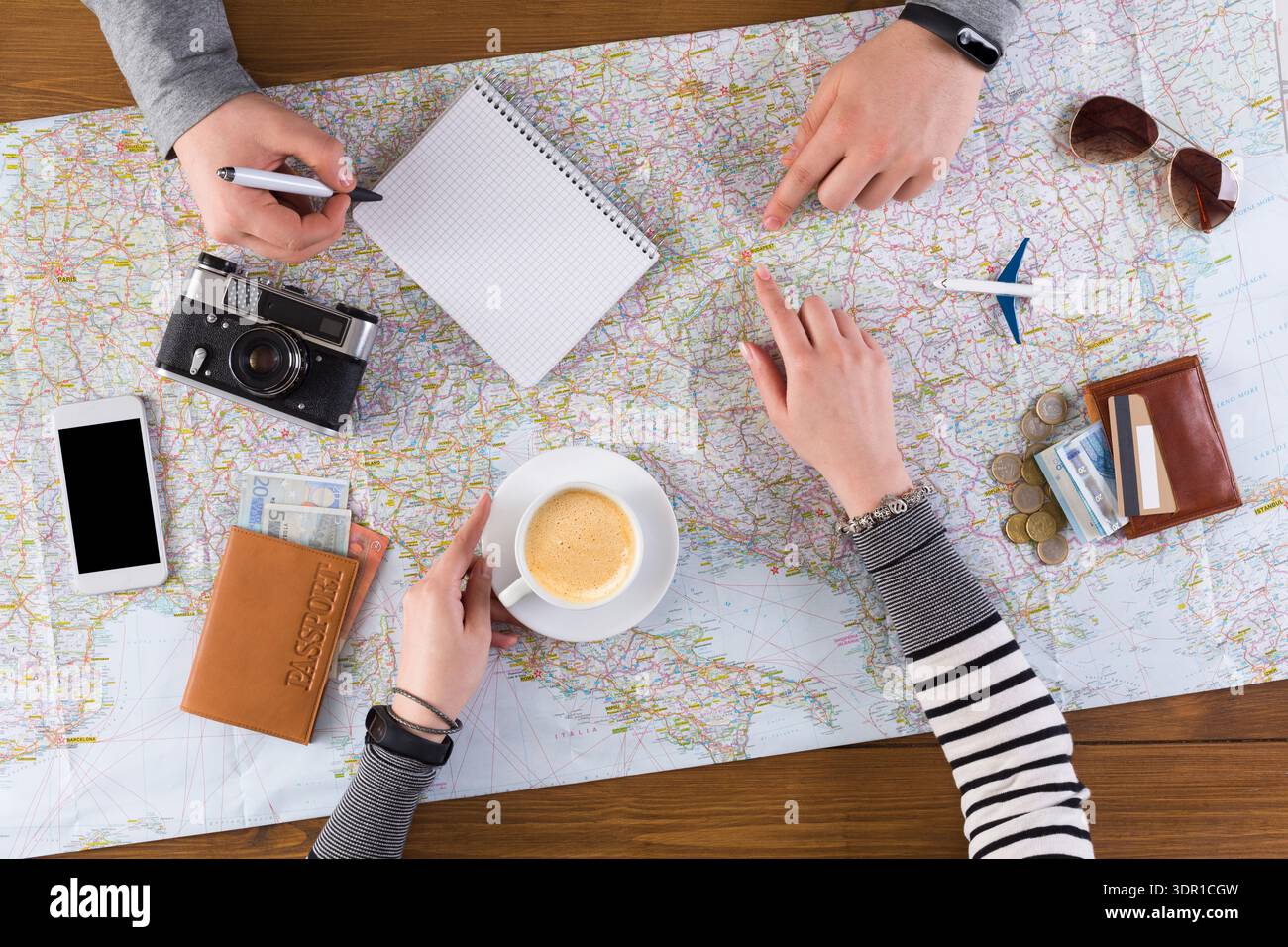 Group Planning a Trip With Map, Notes, and Coffee on a Wooden Table Stock Photo
